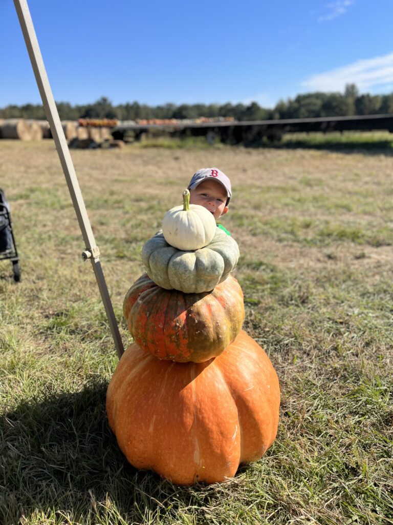 Kid hiding behind large, stacked pumpkins